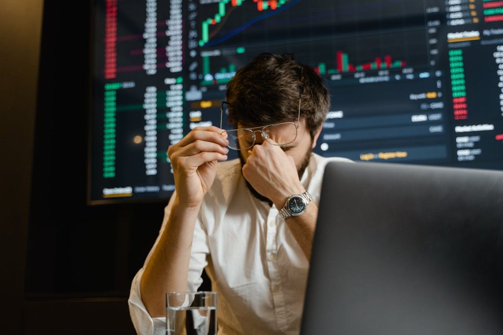 A stressed man looks at stock market data on his computer screen in an office setting.